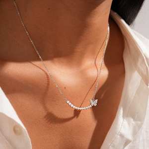 Detail of silver pearl necklace with butterfly pendant on model neckline