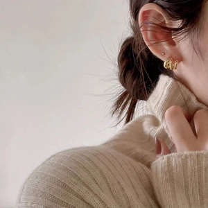 Close-up of minimalist gold twisted hoop earrings worn by a model in a cozy knit sweater