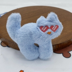 Close-up of a light blue plush cat brooch with heart-shaped eyes on a wooden tray