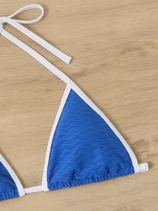 Detail view of blue wavy textured bikini top with white contrast trim on wood background