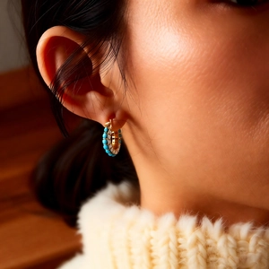 Detail of gold-plated hoop earrings with blue turquoise beads and sparkling zircons