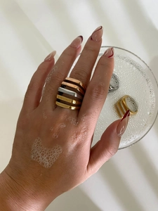 Detail of stacked gold, silver and rose gold hollow geometric rings on hand and in glass