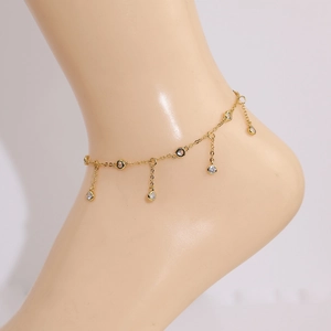 Close-up of a delicate gold anklet with sparkling round zircon charms on a woman's ankle
