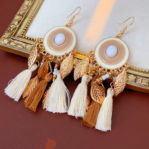 Close-up of vintage bohemian enamel earrings with leaf charms and silk tassels