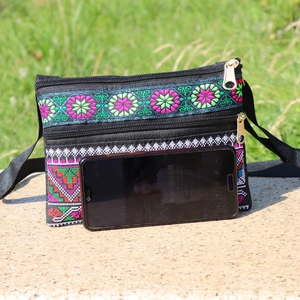Ethnic embroidery crossbody bag with dual gold zippers and adjustable strap on stone surface