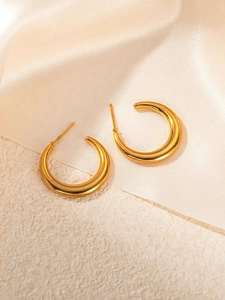 Macro detail of high-polish C-shaped gold hoop earrings on satin material