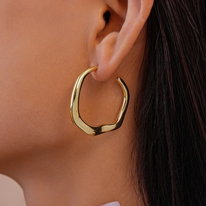 Close-up of golden irregular geometric hoop earring with liquid metal texture on ear
