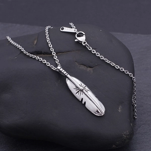 Macro detail of silver feather pendant in stainless steel with sunburst engraving on stone