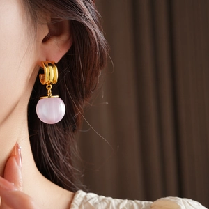 Close-up of golden hoop earrings with translucent pink spherical charms on a model