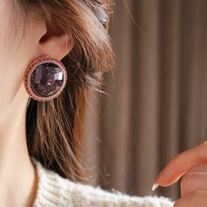 Close-up of model wearing large purple resin earring with pink crystal border