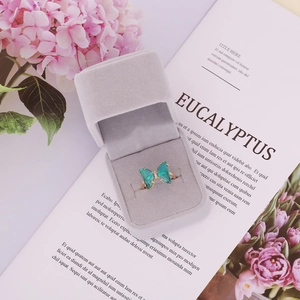 Detail of a gold butterfly ring with green glass wings in a grey velvet jewelry box