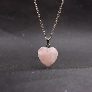 Close-up of heart-shaped pink crystal pendant on a silver chain over a black background