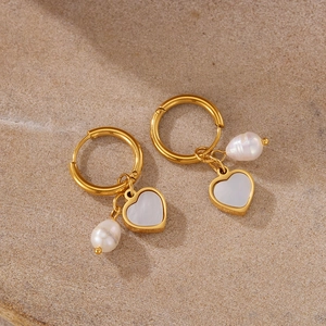 Macro view of golden hoop earrings featuring white heart shell and baroque pearl charms