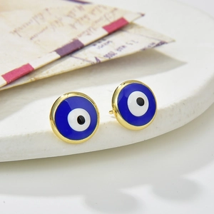 Detailed view of gold-plated blue evil eye stud earrings on a white display stand