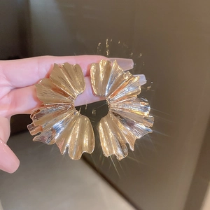 Macro shot of large golden flower petal earrings with textured metal finish details