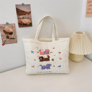 Detail shot of white quilted tote bag featuring colorful cat embroidery and Luck slogan