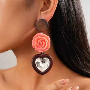 Détail d'une boucle d'oreille bohème avec clou en bois, rose en résine et cœur en cristal