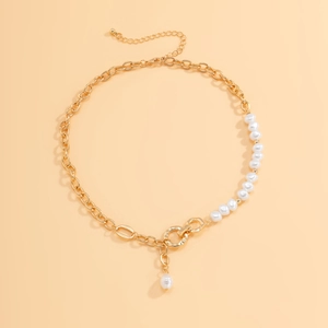 Close-up of asymmetric gold chain and pearl necklace with round pendant on orange backdrop