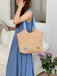 Detail of woven straw shoulder bag featuring colorful knit bows and a light blue strap