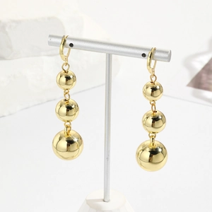 Close-up of three-tier golden sphere drop earrings with high-polish finish on a white stand