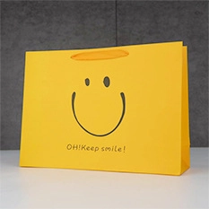 Detail of yellow paper gift bag featuring a black smile logo and flat ribbon handle