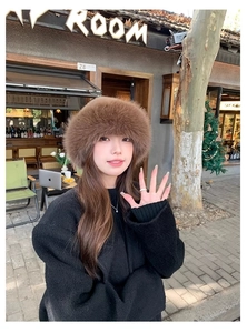 Outdoor shot of a brown faux fur bucket hat styled with a black oversized coat