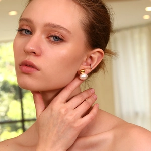 Close-up of model wearing 18K gold plated stud earrings with small pearls and a black ear cuff