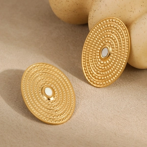 Macro detail of golden oval hammered earrings with white stone inlay on beige background