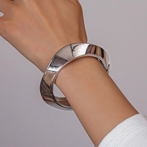 Close-up of a wide polished silver cuff bracelet with a twisted geometric design