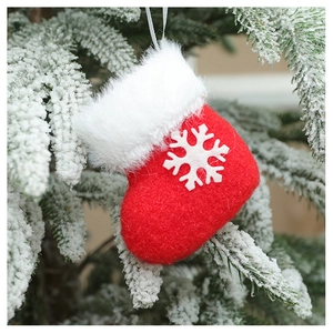 Detail of red plush Christmas sock ornament with white snowflake on snowy pine branch