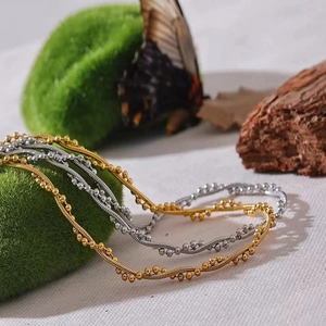 Layered gold and silver snake bead chain necklace displayed on moss and wood