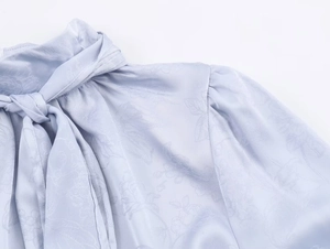 Detail der hellblauen Satinbluse mit Jacquard-Muster, Schleifenausschnitt und Faltenwurf