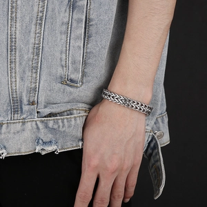 Close-up of a men's silver stainless steel woven chain bracelet with a lion head charm