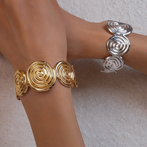 Close-up of gold and silver spiral geometric bangles worn on wrists over a textured background