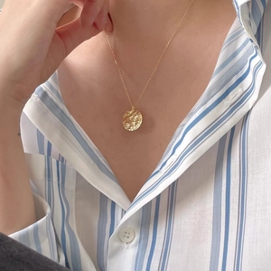 Model wearing a gold round pendant necklace with hammered texture finish on stripe shirt