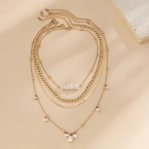 Detail of layered gold necklace set featuring snake chain, curb chain and faux pearls
