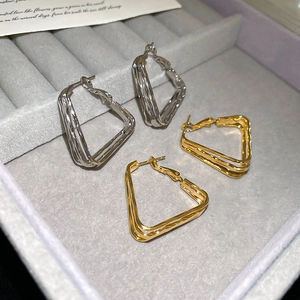 Detailed view of 18k gold and silver geometric multi-layer hoop earrings on a tray