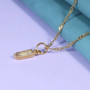 Detailed close-up of a gold rectangular pendant with clear zircon on soft fabric