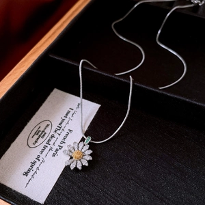Macro detail of silver daisy pendant necklace with yellow gems on black velvet case