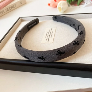 Detail of grey wide fabric headband featuring black bow patterns and handmade label