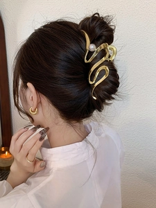 Detailed view of a gold metal hair claw with pearls styled in a sleek bun on a model