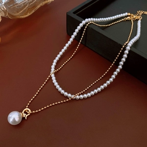 Détail d'un collier double rang en perles et chaîne dorée sur fond de cuir bordeaux