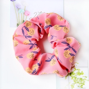 Detailed view of pink fabric scrunchie with orange fruit and blue leaf patterns