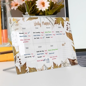 Close-up of clear acrylic weekly planner board with autumn leaf design and metal stand