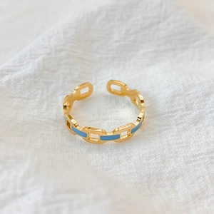 Close-up of gold chain link ring with sky blue enamel details on white fabric