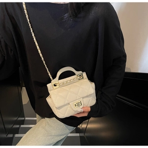 Detail of quilted beige crossbody bag featuring gold twist lock and chain strap on a black top