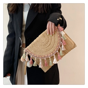 Detail view of khaki straw clutch featuring multi-color tassels and hand-woven texture