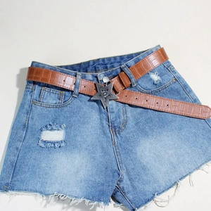 Detail der Vintage Silberstern Schnalle auf braunem Krokodilleder Gürtel und Denim Shorts