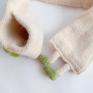 Close-up of soft beige knitted scarf texture with decorative green knit accents