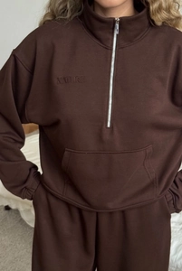 Close-up of NATURE embroidery on brown half-zip sweatshirt with kangaroo pocket detail